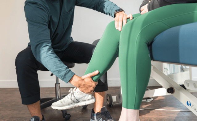 A physiotherapist demonstrating leg exercises to a patient, focusing on calf and Achilles tendon stretches in a modern clinic setting.